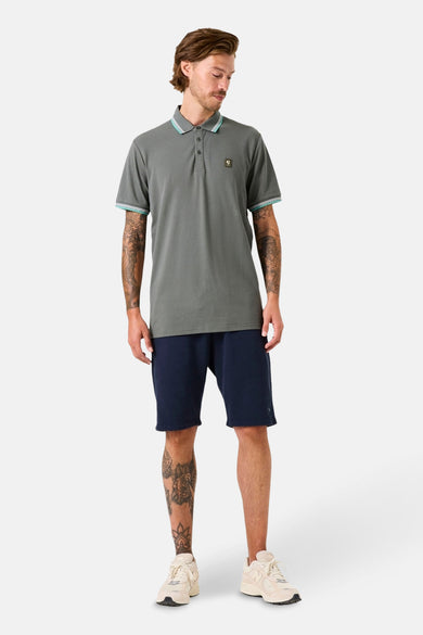 Polo kaki à manches courtes de GARCIA, avec finitions rayées au col et aux manches, porté avec un short bleu marine.