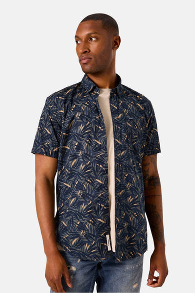 Chemise à manches courtes bleue à motif de feuilles par GARCIA, portée sur un t-shirt écru et un jean déchiré.