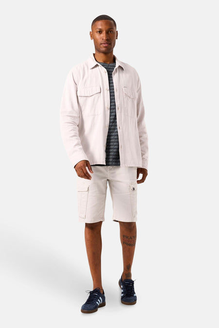 Bermuda gris de GARCIA, porté avec une chemise beige et des chaussures de sport bleu marine.