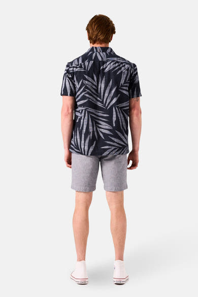 Bermuda bleu de GARCIA, avec une texture chinée, porté avec une chemise à motifs de feuilles.