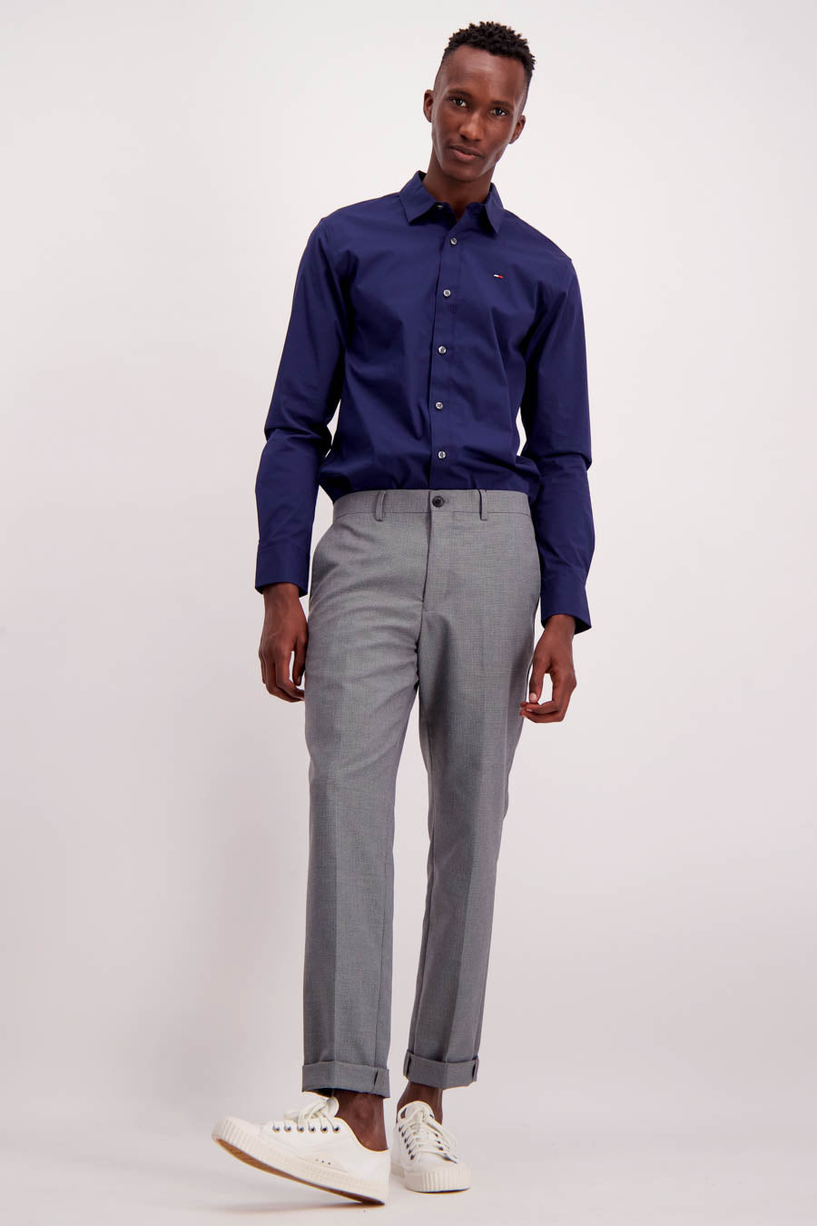 Chemise à manches longues bleue de Tommy Jeans, portée avec un pantalon gris et des chaussures blanches.