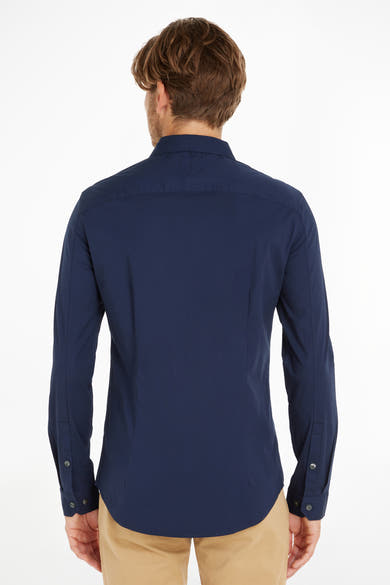 Chemise bleue à manches longues de Tommy Jeans, vue de dos, portée avec un pantalon beige.