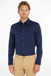 Chemise à manches longues bleue de Tommy Jeans, avec des boutons et portée avec un pantalon beige.
