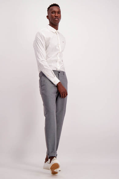 Chemise blanche à manches longues de Tommy Jeans, avec une coupe classique et un col boutonné, portée avec un pantalon gris.