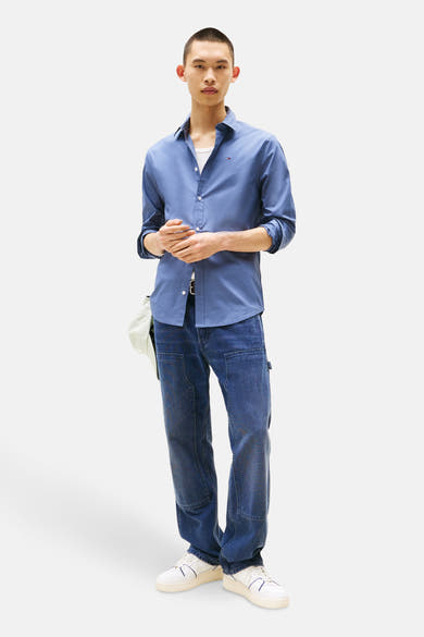 Blauwe blouse met lange mouwen van TOMMY JEANS, gedragen met een witte tanktop en een casual spijkerbroek.