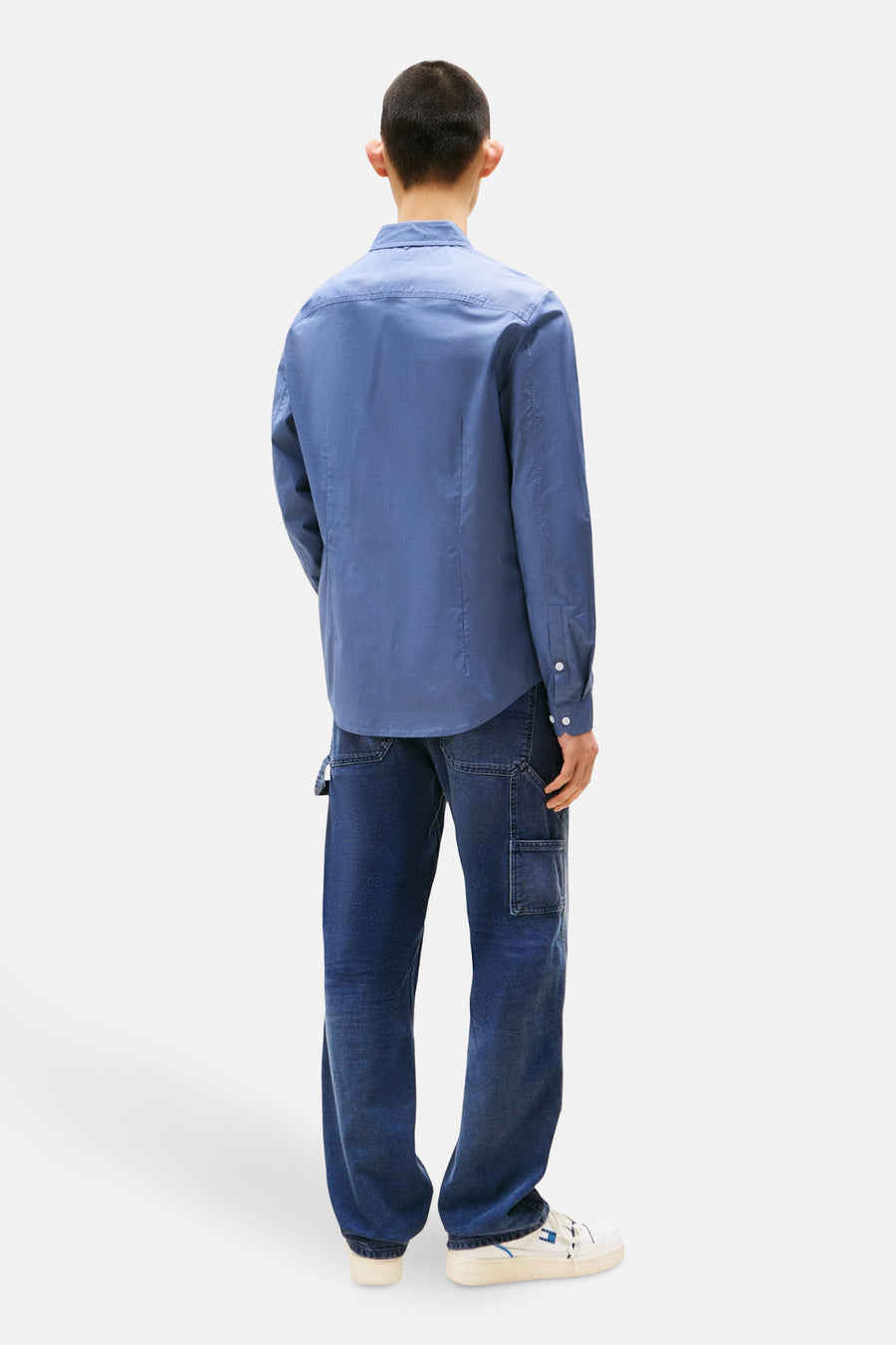Chemise à manches longues bleue de TOMMY JEANS, portée avec un pantalon cargo en denim et des baskets blanches, vue de dos.
