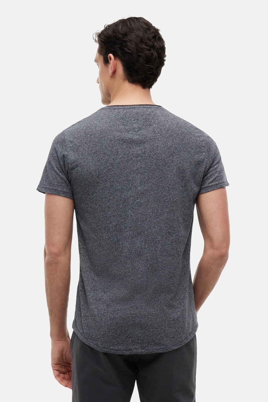 T-shirt gris chiné de Tommy Jeans, vue de dos sur un homme portant un short foncé, avec un petit logo brodé au cou, manches courtes et ourlet incurvé.