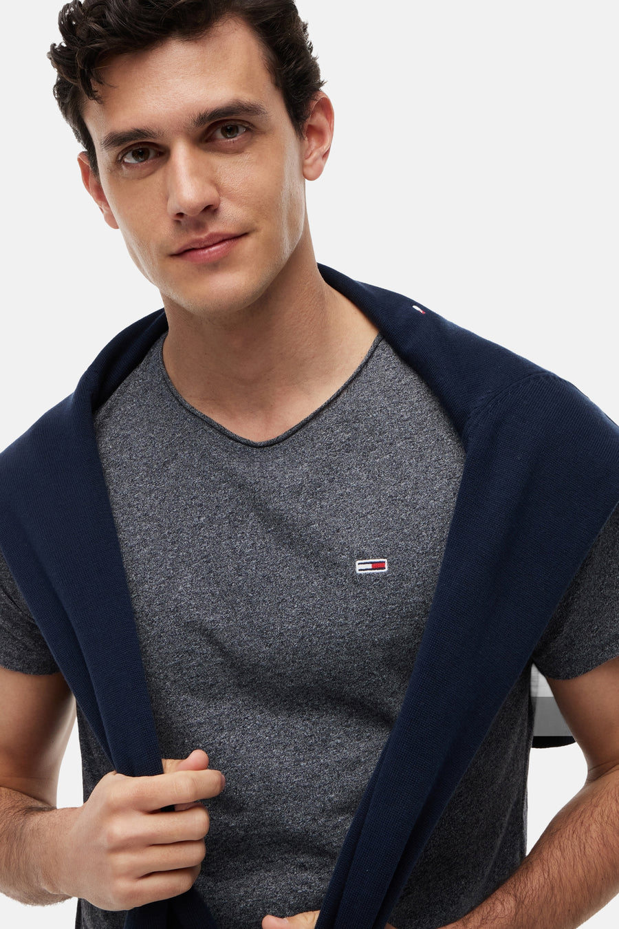 T-shirt gris chiné à col en V de Tommy Jeans, avec un petit logo et un pull bleu marine sur les épaules.