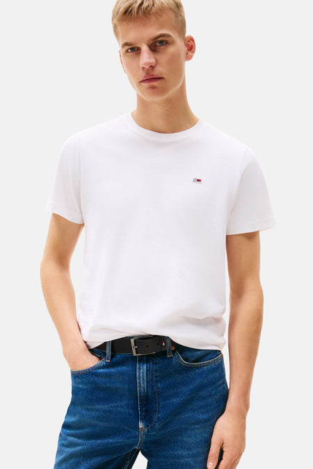T-shirt blanc de TOMMY JEANS porté avec un jean bleu et une ceinture noire.
