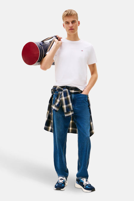 T-shirt blanc de TOMMY JEANS, porté avec un pantalon en jean bleu et une chemise à carreaux nouée.