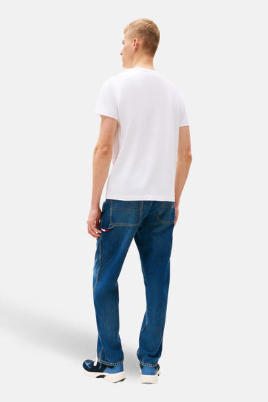 T-shirt blanc de TOMMY JEANS, porté avec un jean bleu et des chaussures de sport.