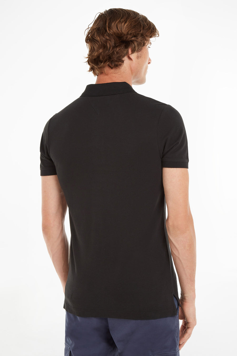 Polo noir de Tommy Jeans, vu de dos, porté avec un pantalon cargo bleu marine.
