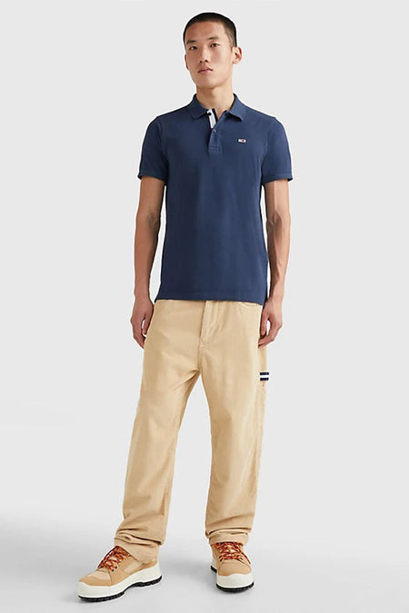 Polo bleu de Tommy Jeans, porté avec un pantalon beige et des baskets montantes.