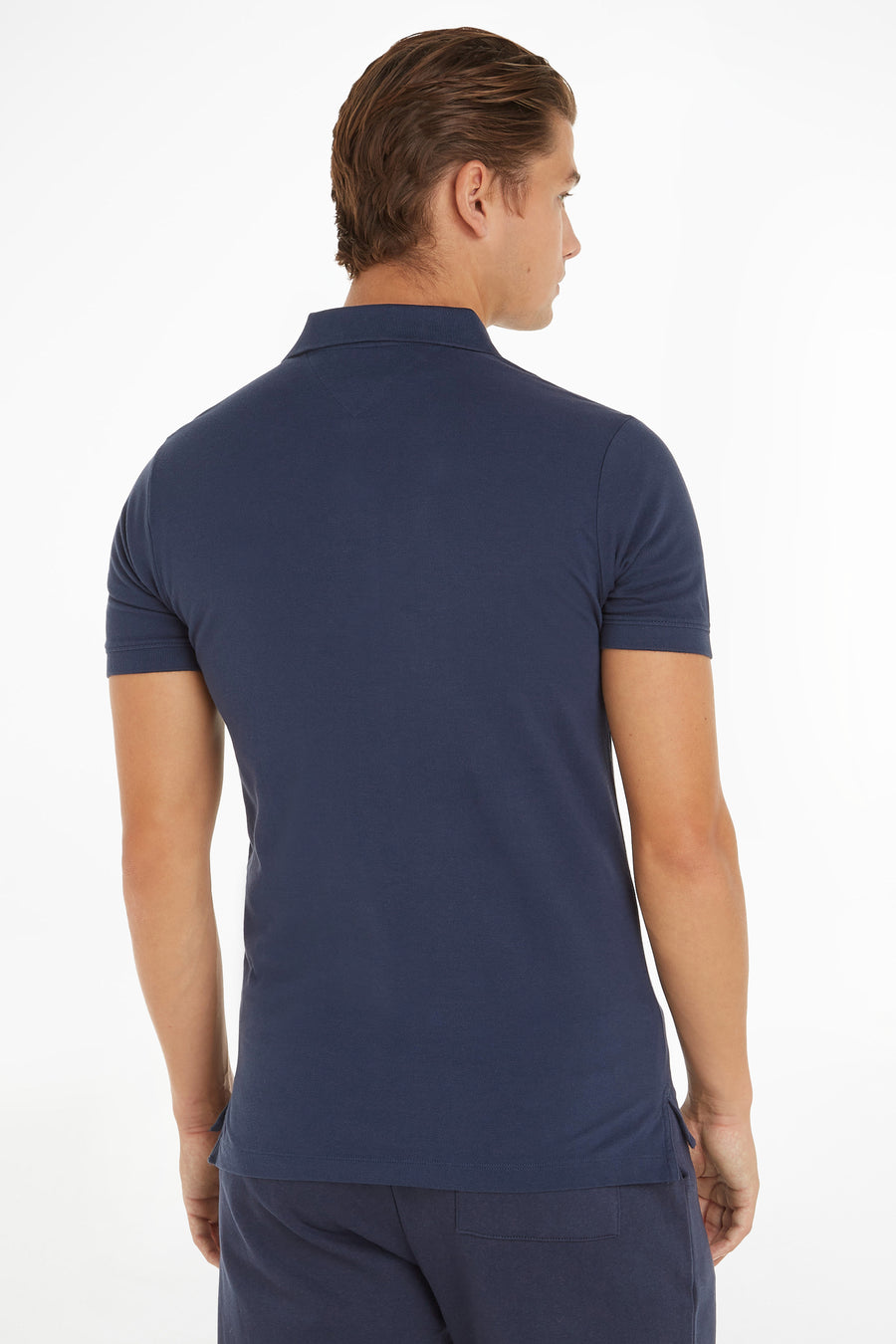 Polo bleu de Tommy Jeans, coupe classique, porté avec un pantalon de survêtement bleu marine, vue de dos.