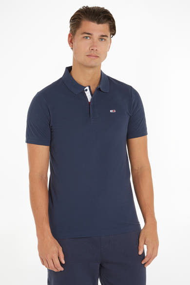 Polo bleu Tommy Jeans avec patte de boutonnage contrastée et logo drapeau sur la poitrine, porté avec un pantalon assorti.