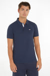 Polo bleu Tommy Jeans avec patte de boutonnage contrastée et logo drapeau sur la poitrine, porté avec un pantalon assorti.
