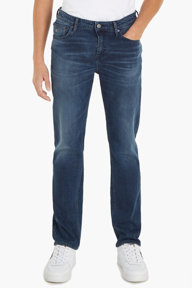 Jean droit en denim bleu foncé de TOMMY JEANS, avec une main dans la poche et des baskets blanches.
