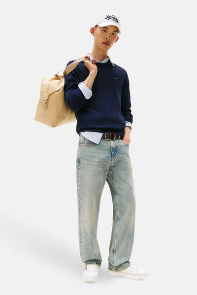 Pull à col rond bleu foncé de Tommy Jeans, porté avec une chemise rayée et un sac beige.