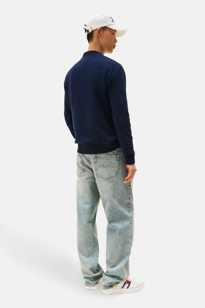 Pull à col rond bleu foncé de TOMMY JEANS, porté avec un jean ample et des baskets blanches.
