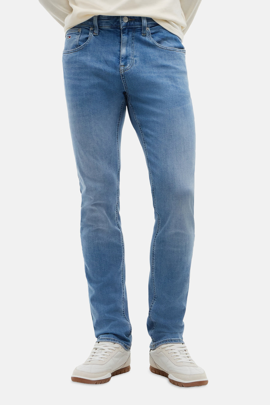 Light blue slim-fit denim jeans by TOMMY JEANS, featuring faded wash and clean stitching, worn with white sneakers.