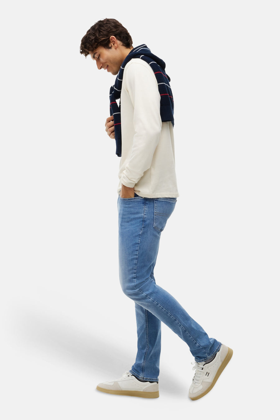 Light blue slim-fit denim jeans by TOMMY JEANS, shown on model in side view with white long-sleeve shirt and white sneakers