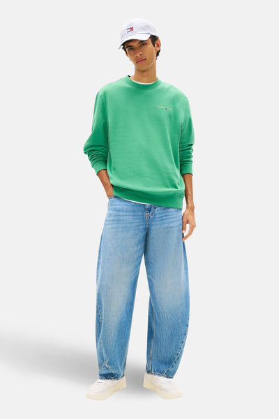 Sweat-shirt col rond vert de Tommy Jeans, porté avec un jean bleu ample et des baskets blanches.