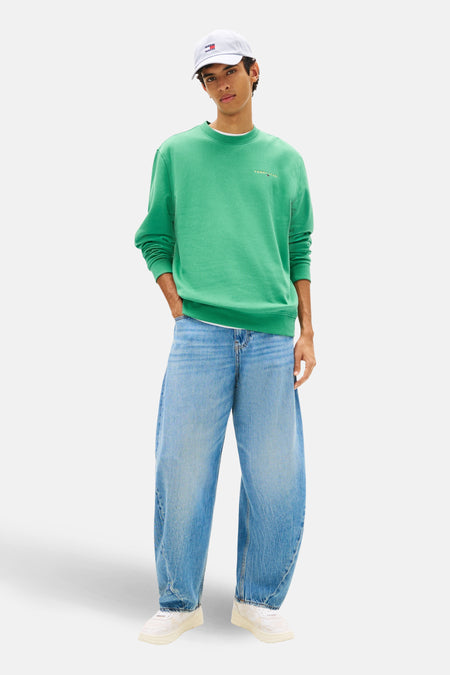 Sweat-shirt col rond vert de Tommy Jeans, porté avec un jean bleu ample et des baskets blanches.