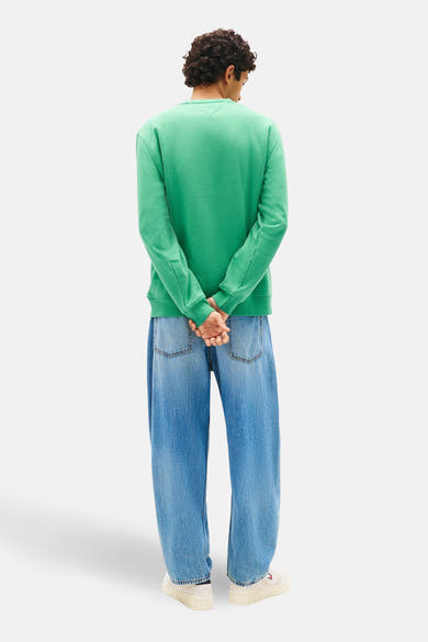 Sweat vert de TOMMY JEANS, porté avec un jean bleu délavé et des baskets blanches, vue de dos.
