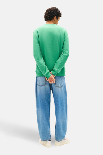 Groene sweater van TOMMY JEANS, gedragen met een lichtblauwe jeans en witte sneakers, achterzijde.