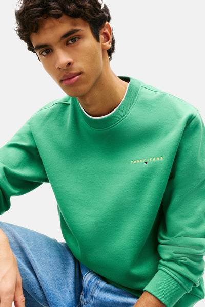 Groene sweater met ronde hals van TOMMY JEANS, met geborduurd logo op de voorkant en gedragen met een blauwe jeans.