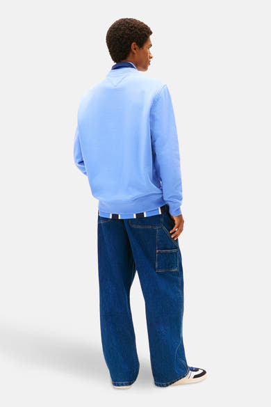 Blauwe sweater van TOMMY JEANS, gedragen met een wijde spijkerbroek met opgestikte zakken.