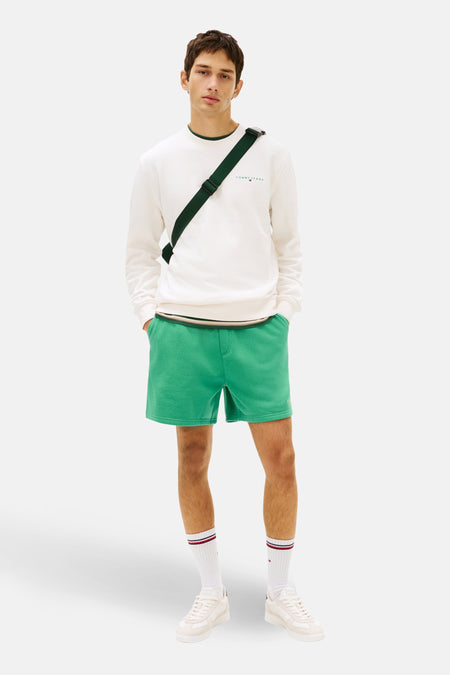 Sweat col rond blanc de TOMMY JEANS, porté avec un short vert et un sac bandoulière.