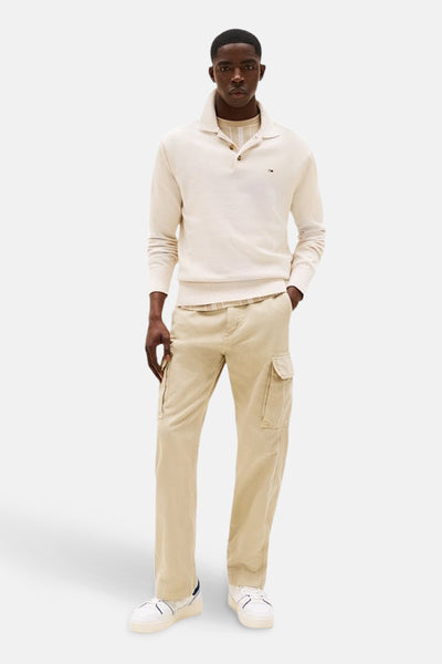 Pull beige en maille fine de TOMMY JEANS, porté sur un t-shirt à rayures, avec un pantalon cargo beige.