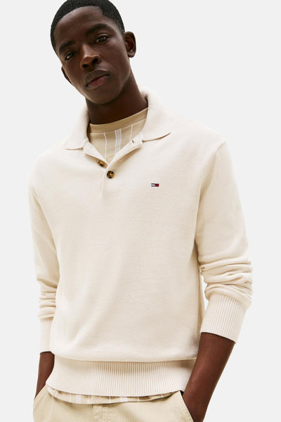 Pull beige à col polo de TOMMY JEANS, avec logo discret et porté sur un t-shirt rayé clair.