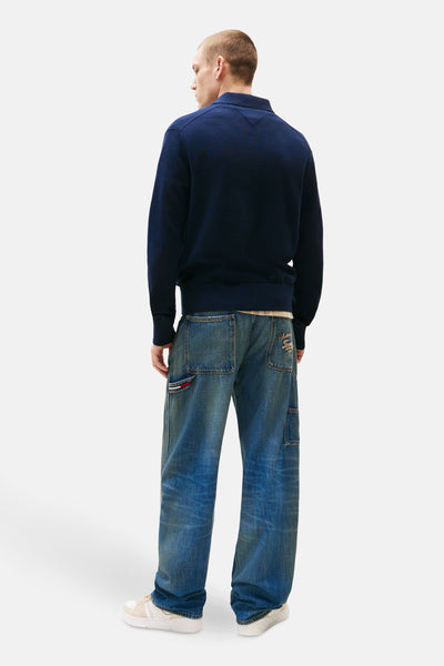 Pull bleu de TOMMY JEANS, porté avec un jean large et des baskets beiges.