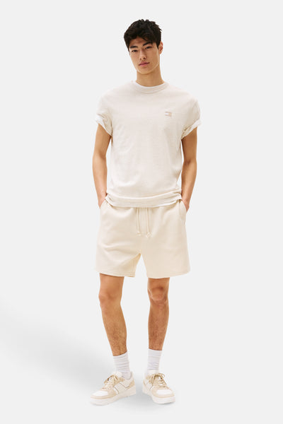 T-shirt beige à manches courtes de TOMMY JEANS, porté avec un short en maille gaufrée et des baskets blanches.