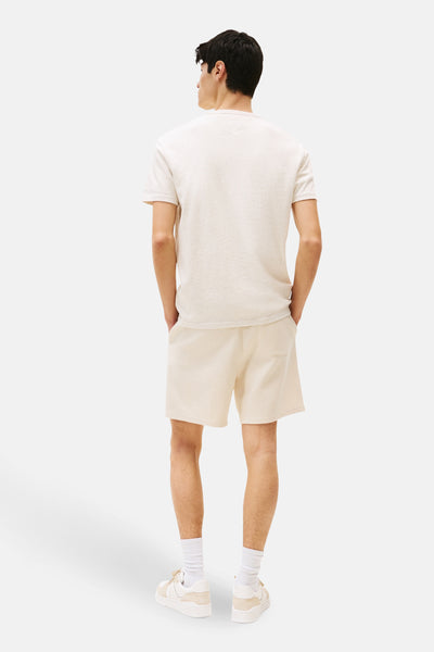 T-shirt beige à manches courtes de TOMMY JEANS, porté avec un short texturé et des baskets crème, vue de dos.
