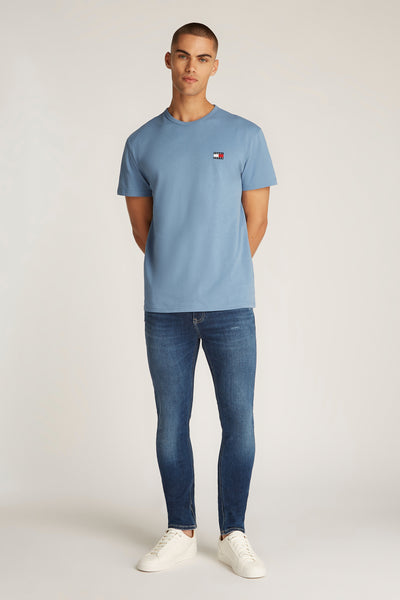 T-shirt à manches courtes bleu de TOMMY JEANS, porté avec un jean bleu et des baskets blanches.