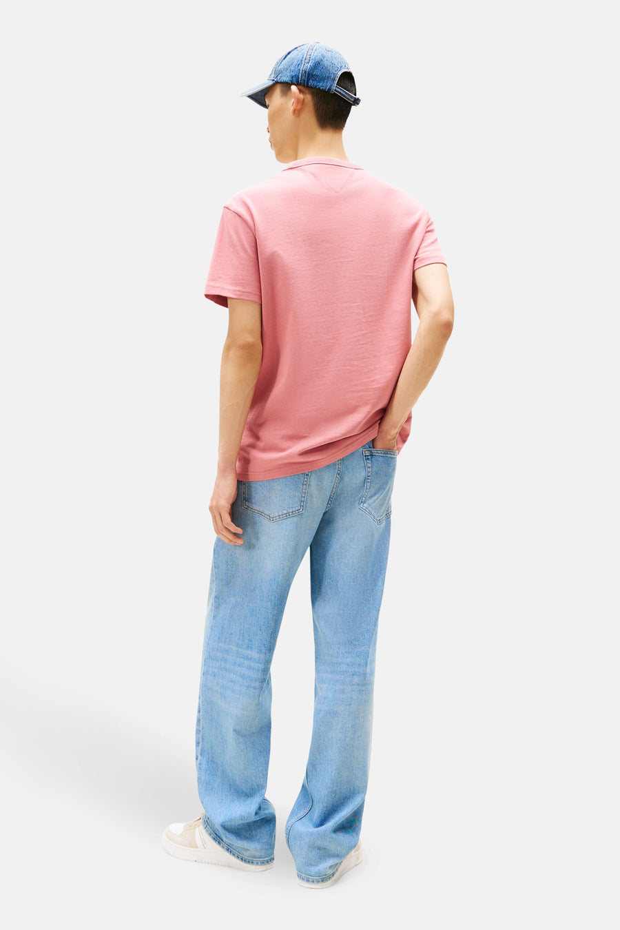 T-shirt à manches courtes rose de TOMMY JEANS, porté avec un jean ample et une casquette en denim, vue de dos.