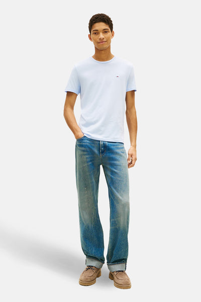 T-shirt à manches courtes bleu de TOMMY JEANS, porté avec un jean délavé et des chaussures marron.