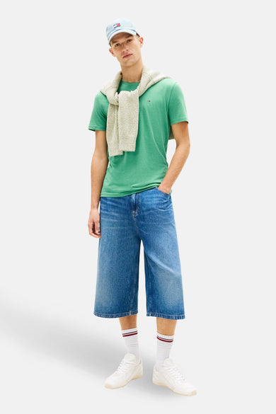 T-shirt vert à manches courtes de Tommy Jeans, porté avec un pull crème noué et un short en jean.