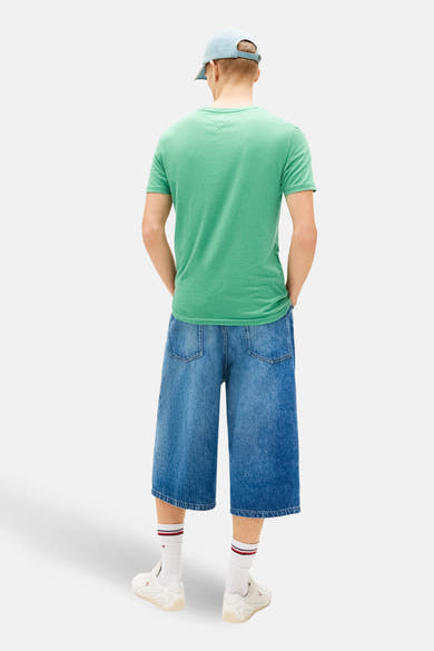 T-shirt à manches courtes vert de TOMMY JEANS, porté avec un short en jean ample et des chaussettes blanches.
