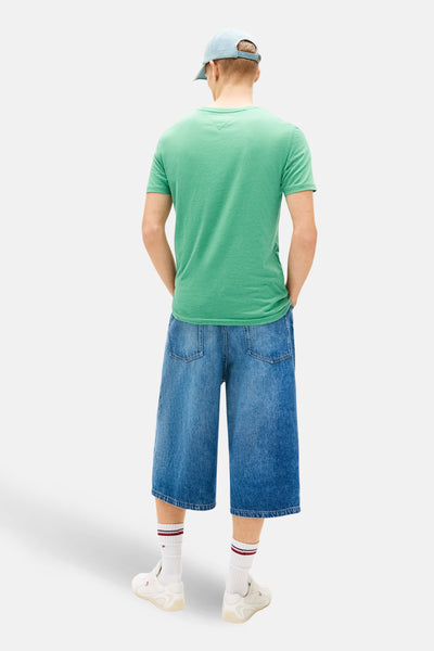 Groen T-shirt met korte mouwen van TOMMY JEANS, gedragen met een wijde spijkerbroek en witte sokken.