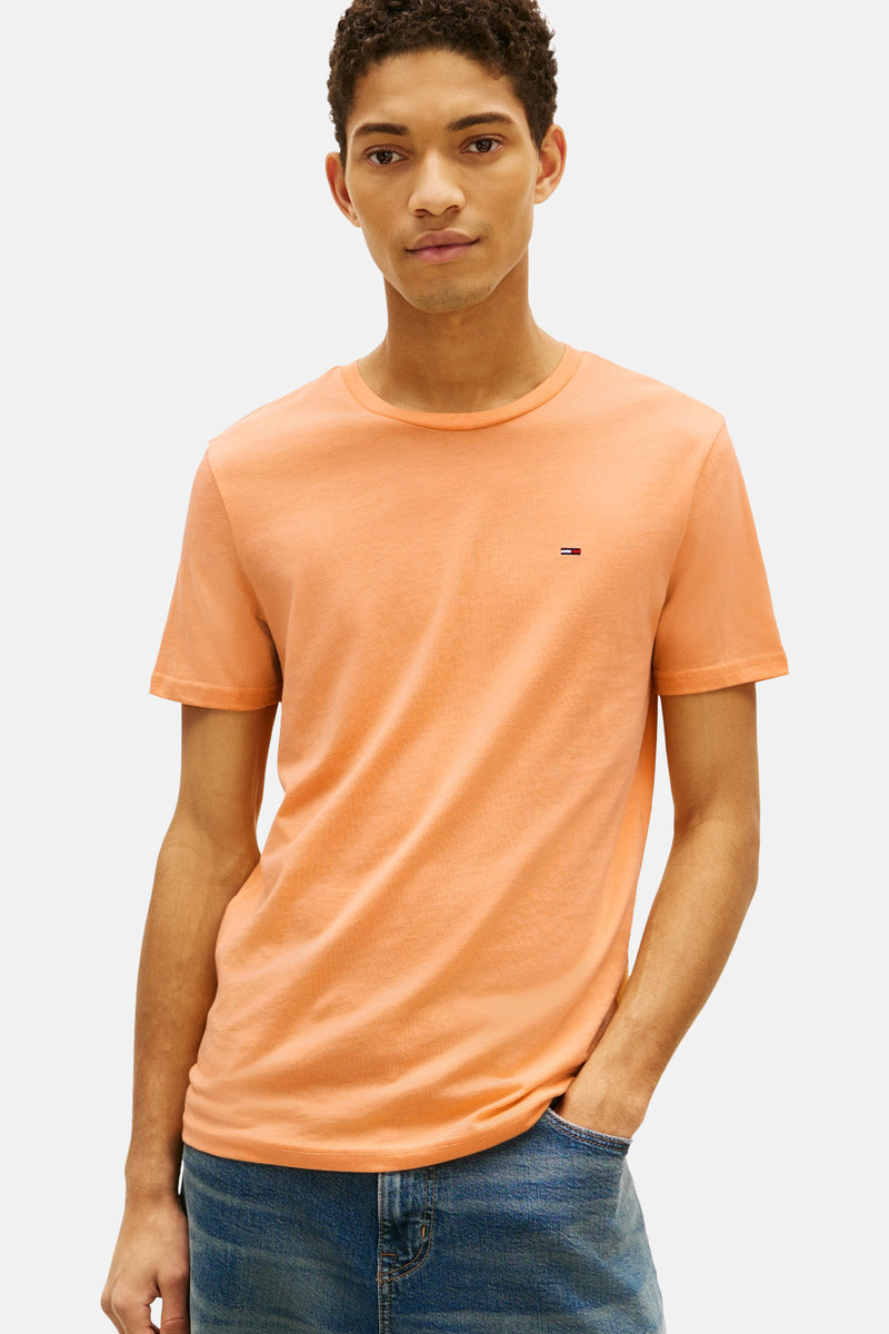 Oranje T-shirt met korte mouwen van TOMMY JEANS, gedragen met een wijde blauwe jeans en witte sneakers.