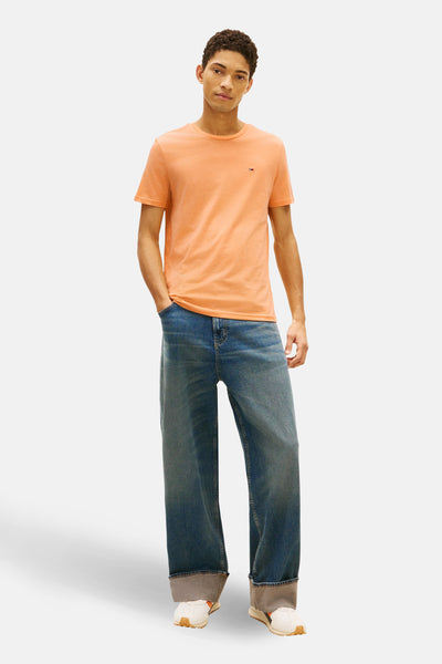 T-shirt orange à manches courtes de TOMMY JEANS, porté avec un jean bleu large et des baskets blanches.