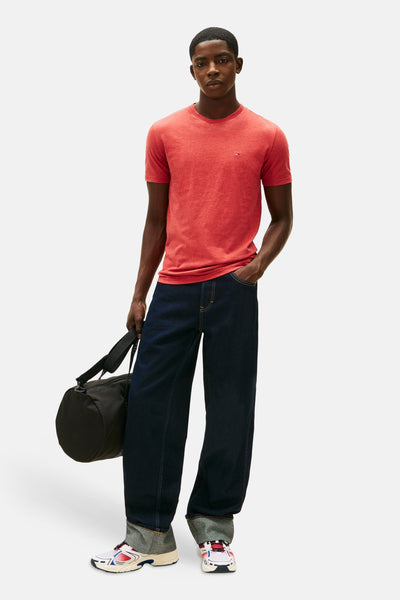 T-shirt rouge à manches courtes de TOMMY JEANS, porté avec un jean large bleu marine et un sac de sport noir.