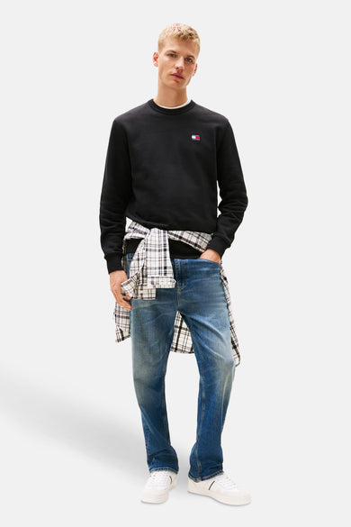 Zwarte sweater van TOMMY JEANS, gedragen met een geruit overhemd dat aan de taille is geknoopt en een spijkerbroek.