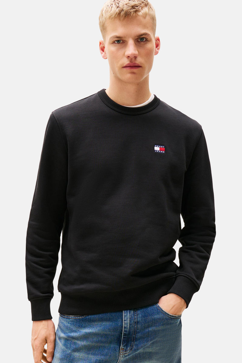 Zwarte sweater van TOMMY JEANS, gedragen met een wit T-shirt en een lichtblauwe spijkerbroek.