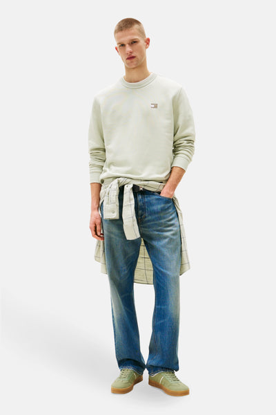 Sweat vert de TOMMY JEANS avec logo sur le devant, porté avec une chemise à carreaux nouée et un jean bleu.