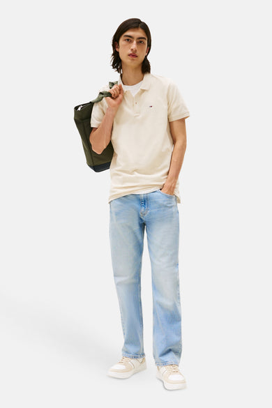 Polo à manches courtes beige de TOMMY JEANS porté avec un jean délavé et un sac vert.
